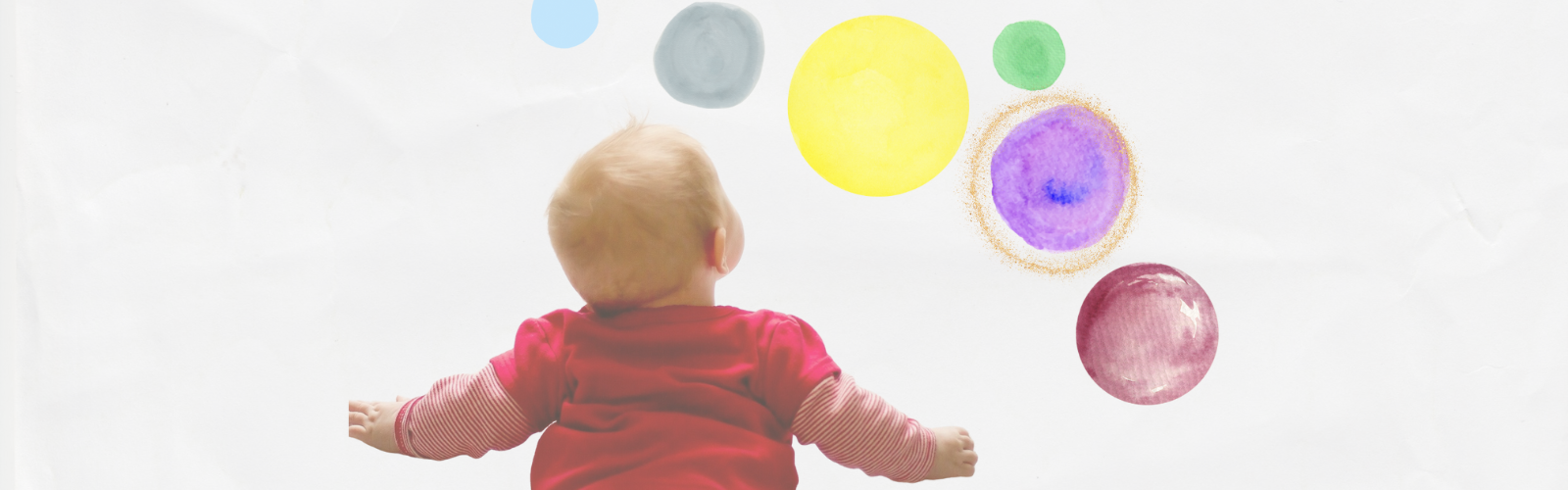 Ein Baby liegt auf dem Bauch und schaut an die Wand mit bunten Farbklecksen.